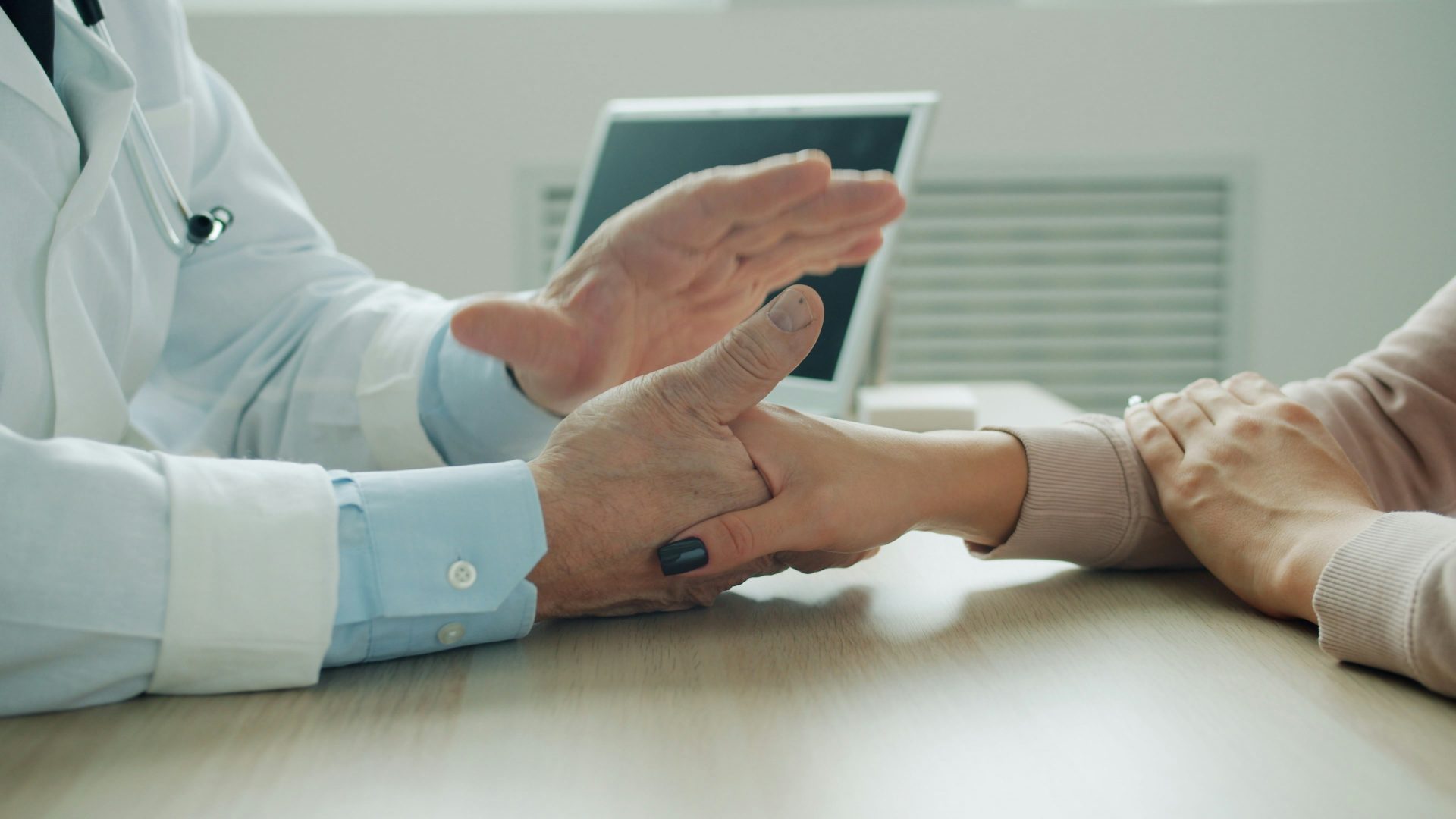 Der Arzt tröstet den Patienten, indem er ihm die Hand auf den Arm legt.